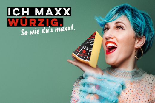 Werbesujet für den Käse «Der scharfe Maxx». Frau mit blau gefärbten Haaren, die Käsestück in der Hand hält.