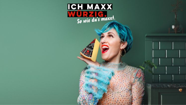 Werbesujet für den Käse «Der scharfe Maxx». Frau mit blau gefärbten Haaren, die Käsestück in der Hand hält.