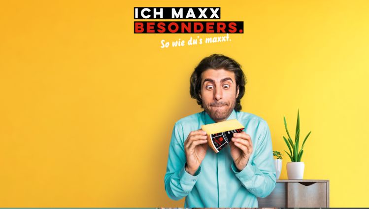 Werbesujet für «Der scharfe Maxx». Junger Mann mit türkisem Hemd hält Käsestück in den Händen.