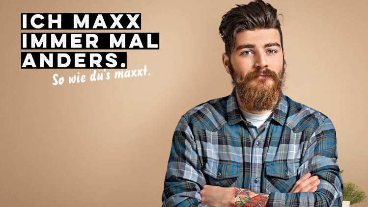 Werbesujet für «Der scharfe Maxx». Junger Mann mit Bart und blaukariertem Hemd.