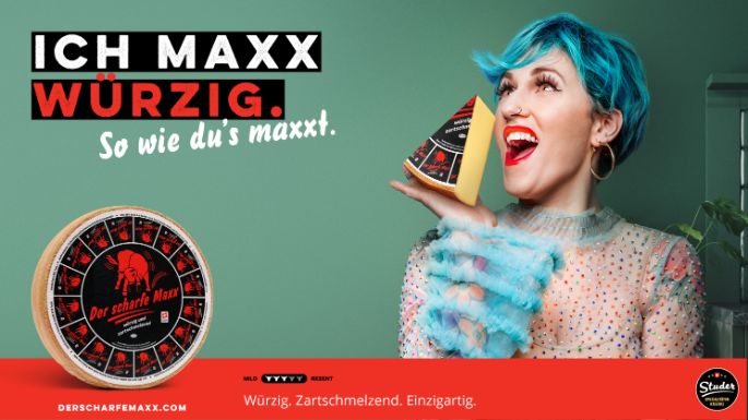 Werbesujet für den Käse «Der scharfe Maxx». Frau mit blau gefärbten Haaren, die Käseecke in der Hand hält.